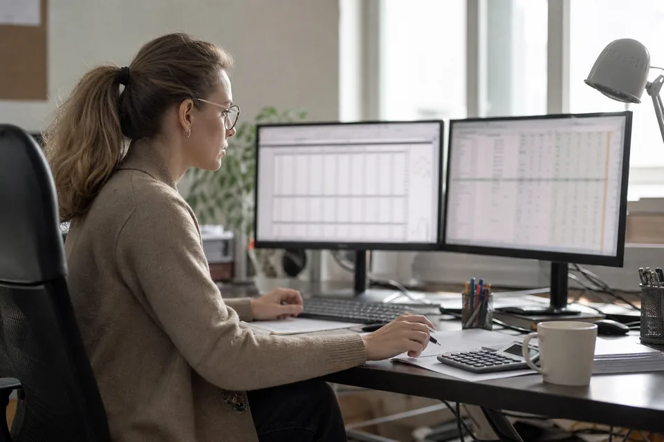 Analityczka porównuje sprawozdania finansowe spółek na dwóch monitorach